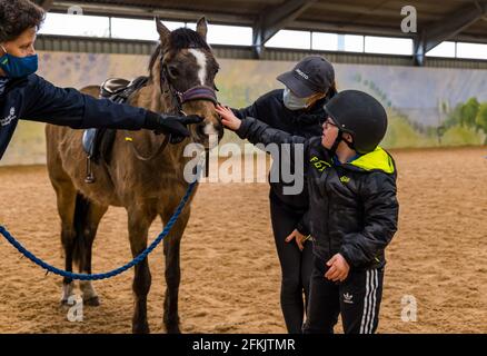 Garçon avec le syndrome de Down patrouiller le cheval avec sa mère portant un masque facial à Riding for Disabled, Muirfield Riding Therapy, East Lothian, Écosse, Royaume-Uni Banque D'Images