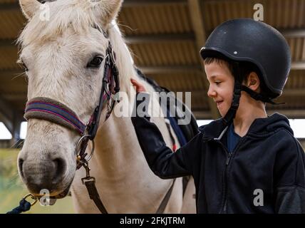 Garçon portant un chapeau d'équitation patting cheval à Riding for Disabled, Muirfield Riding Therapy, East Lothian, Écosse, Royaume-Uni Banque D'Images