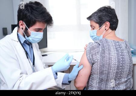 Médecin vaccinant la patiente adulte en clinique. Infirmière tenant la seringue avant d'injecter le vaccin Covid-19 ou le coronavirus. Banque D'Images