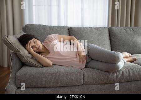 Une femme enceinte malsaine qui s'est allongée sur un canapé et qui a de la douleur Banque D'Images