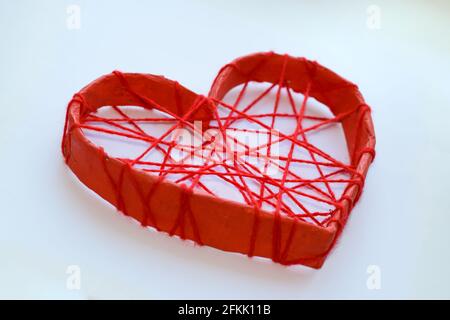 Un coeur en papier attaché avec des fils rouges. Cœur sur fond blanc. Banque D'Images