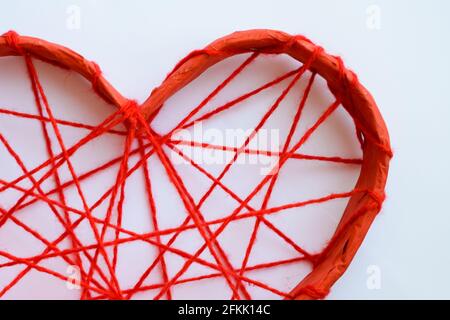 Un coeur en papier attaché avec des fils rouges. Cœur sur fond blanc. Banque D'Images