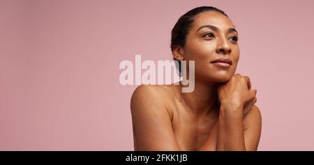Jolie femme avec une peau saine regardant loin. Race mixte femelle sur fond rose. Banque D'Images