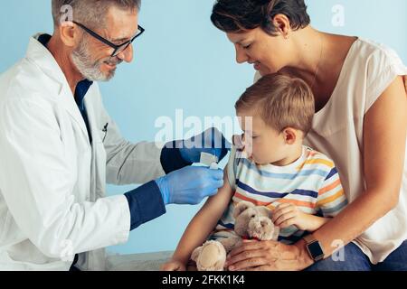 Médecin appliquant un aide-bande sur le bras d'un garçon après lui avoir donné un vaccin contre la grippe. Garçon assis avec sa mère se faire vacciner. Banque D'Images