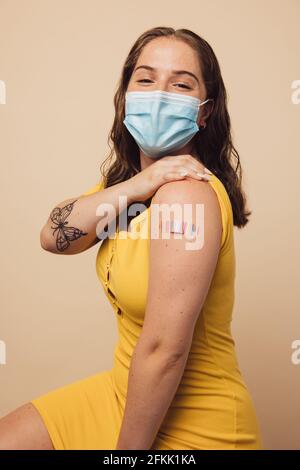Jeune femme montrant son bras avec bandage après vaccination. Femme portant un masque protecteur après avoir reçu le vaccin contre le covid. Banque D'Images