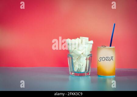 Verre rempli de cubes de sucre et de soda bidon avec paille bleue près de rose fond rétro design, malsain nourriture, la malbouffe, concept de bonbons avec l'espace de copie Banque D'Images