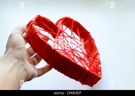 Coeur en carton et avec des fils rouges dans la main d'un homme. Un coeur en papier attaché avec des fils rouges. Cœur sur fond blanc. Banque D'Images