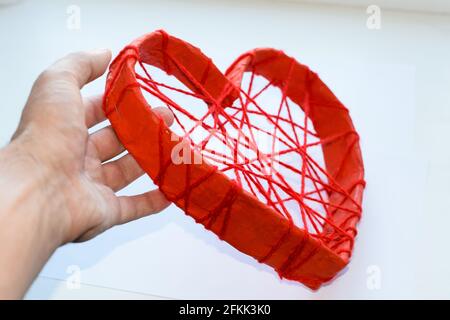 Coeur en carton et avec des fils rouges dans la main d'un homme. Un coeur en papier attaché avec des fils rouges. Cœur sur fond blanc. Banque D'Images