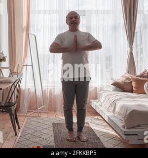 Homme senior pratiquant le yoga à la maison faisant pose de chaise, Utkatasana Banque D'Images