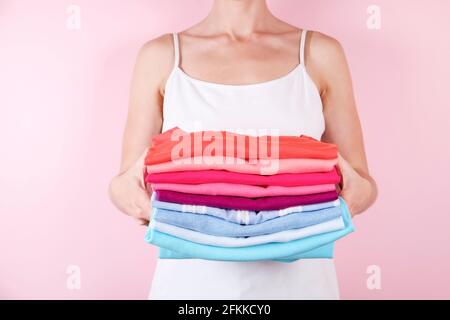 Gros plan d'une jeune femme attrayante tenant une pile de chemises multicolores parfaitement pliées. Femme avec pile de vêtements de différentes couleurs dans ses mains sur pal Banque D'Images