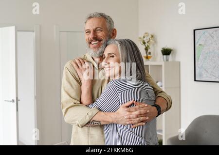 Heureux couple mûr qui s'embrasse, regarde loin, pense, rêve de l'avenir à la maison. Banque D'Images