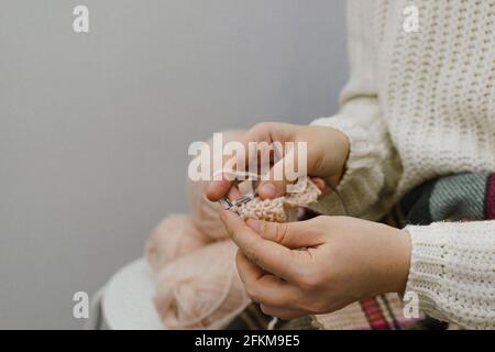 Les mains des femmes tricotées à partir de fils de couleur chair, fond gris. Banque D'Images