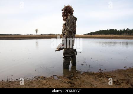waterfowler avec un leurre de canard dans sa main est sur l'eau peu profonde Banque D'Images