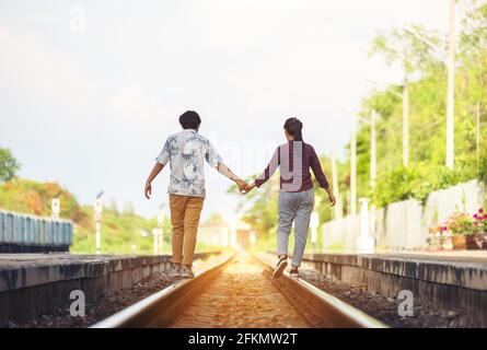 Jeune couple marchant main dans la main sur les voies de chemin de fer, le long de l'ensemble de chemin de fer Banque D'Images