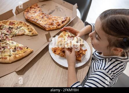 Une adorable petite fille mange une tranche de pizza pour le déjeuner. Banque D'Images