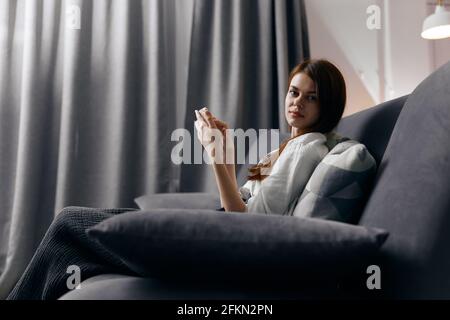 vue latérale d'une femme aux cheveux rouges avec téléphone assis sur un canapé Banque D'Images