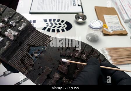 Un scientifique de police prend des échantillons d'une semelle de chaussure dans un laboratoire de crime, image conceptuelle Banque D'Images