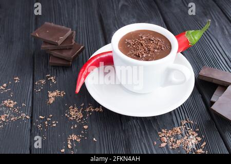 Chocolat chaud dans la tasse blanche et piment rouge sur fond de bois noir. Gros plan. Banque D'Images