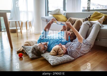 Beau couple heureux mature utilise une tablette numérique, parler et sourire à la maison Banque D'Images