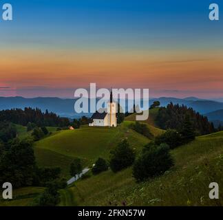 Sveti Andrej, Slovénie - église Saint Andrew (SV. Andrej) au coucher du soleil dans la région de Skofja Loka avec les Alpes juliennes et le ciel coloré en arrière-plan. Heure d'été i Banque D'Images