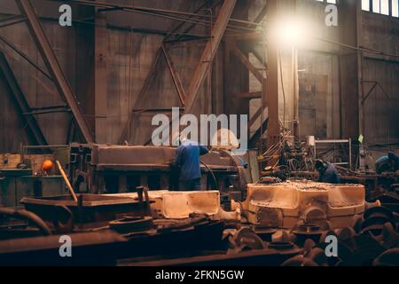 Le travailleur en atelier traite de grandes pièces de fonte après moulage dans une usine de fonderie métallurgique. Banque D'Images