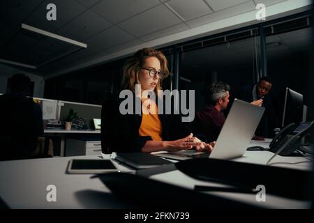 Jeune femme d'affaires blonde travaillant sérieusement sur un ordinateur portable dans un bureau moderne Banque D'Images