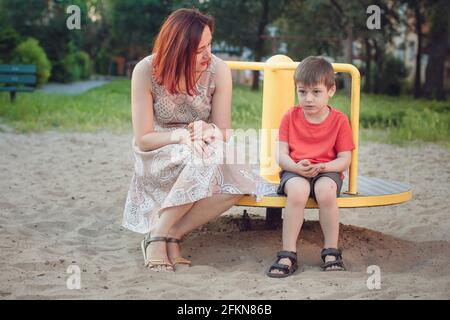 Maman et son fils sur l'aire de jeux. Garçon en T-shirt rouge vif et jeune femme en robe à l'extérieur l'été. La vie quotidienne. Concept de l'enfance et de la relation de Banque D'Images