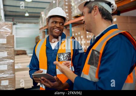 Un employé africain qui regarde son superviseur à l'intérieur d'une tablette numérique la main à l'entrepôt Banque D'Images