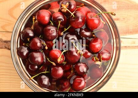 Plusieurs cerises douces et juteuses rouge foncé dans un plat de verre sur une table en bois, vue rapprochée, vue de dessus. Banque D'Images