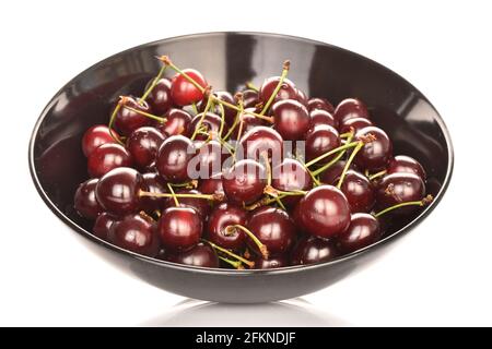 Plusieurs cerises sucrées et juteuses rouge foncé dans un plat de poterie noir, en gros plan, isolées sur du blanc. Banque D'Images