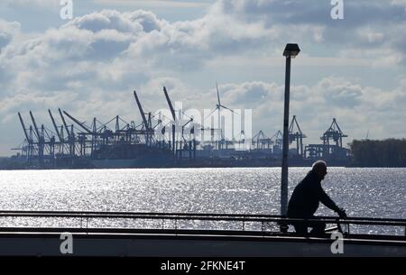 Hambourg, Allemagne. 03ème mai 2021. Un homme traverse un pont à vélo sur la jetée de Teufelsbrück ; les grues sur portique à conteneurs du terminal à conteneurs Burchardkai sont visibles en arrière-plan. De grands navires à conteneurs peuvent desservir le port de Hambourg avec un tirant d'eau augmenté jusqu'à 0.9 M. Après près de deux ans de construction, le transport maritime peut profiter des nouvelles profondeurs du fairway d'Elbe. Credit: Marcus Brandt/dpa/Alay Live News Banque D'Images