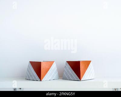 Pots en béton de bricolage vides, forme pyramidale sur une étagère en bois blanc sur fond de mur blanc avec espace de copie. Deux ciment unique peint couleur cuivre plante Banque D'Images