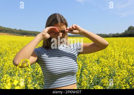 Femme stressée rayant les yeux qui démangent dans un champ de récolte dans saison de printemps Banque D'Images