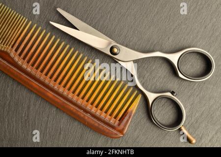 Ciseaux métalliques avec un peigne en plastique sur une planche d'ardoise. Banque D'Images