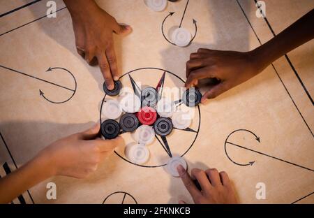 Focus sur les pièces de monnaie, vue du dessus des mains multiethniques pour enfants arranger les pièces de jeu de carrom pour jouer au match - concept des activités de loisirs, le travail d'équipe Banque D'Images