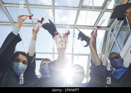 Vue de haut niveau d'un groupe de diplômés universitaires titulaires de diplômes en position debout à l'intérieur, éclairé par la lumière du soleil Banque D'Images