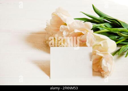 Composition féminine avec bouquet de tulipes blanches et carte de vœux vierge. Beau bouquet pour la fête de la mère sur table, livraison de fleurs, ho de printemps Banque D'Images