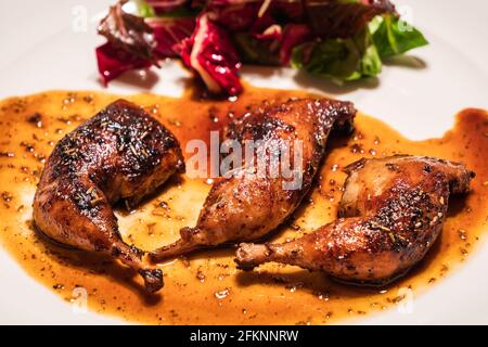 Pattes de caille poêlées au jus de Madère, herbes et salade sur une assiette blanche Banque D'Images