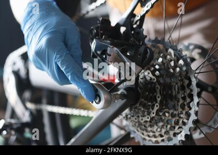 Un homme de main en gants de caoutchouc répare la bicyclette en atelier Banque D'Images