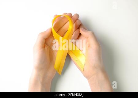 Main de femme tenant un ruban jaune - symbole de sensibilisation au cancer de la vessie, du foie et des os. Concept de prévention du cancer chez les enfants. Arrière-plan isolé, copier sp Banque D'Images