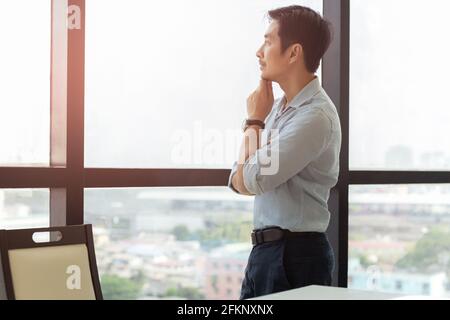 Homme d'affaires asiatique attentionné, situé à côté d'une grande fenêtre. Banque D'Images