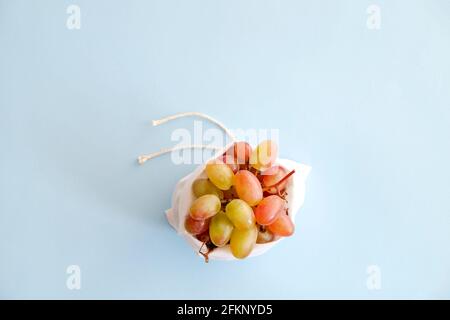 Sac réutilisable en coton à nouer écologique garni de branches de raisin biologique sur fond bleu clair. Concept zéro déchet. Vue de dessus Banque D'Images