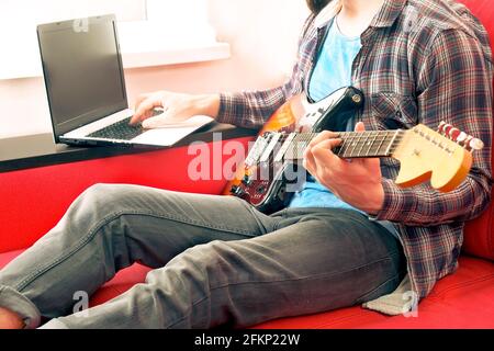 Jeune homme, chanteur de folk hippster auteur-compositeur en chemise à carreaux, jouant de la guitare électrique offset Sunburst. Guitariste mâle prenant de la musique jazz en ligne c Banque D'Images