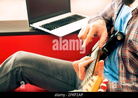 Jeune homme, chanteur de folk hippster auteur-compositeur en chemise à carreaux, jouant de la guitare électrique offset Sunburst. Guitariste mâle prenant de la musique jazz en ligne c Banque D'Images