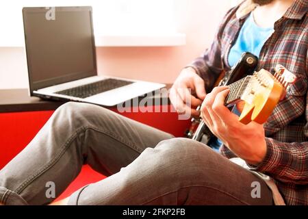 Jeune homme, chanteur de folk hippster auteur-compositeur en chemise à carreaux, jouant de la guitare électrique offset Sunburst. Guitariste mâle prenant de la musique jazz en ligne c Banque D'Images