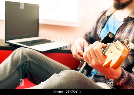 Jeune homme, chanteur de folk hippster auteur-compositeur en chemise à carreaux, jouant de la guitare électrique offset Sunburst. Guitariste mâle prenant de la musique jazz en ligne c Banque D'Images