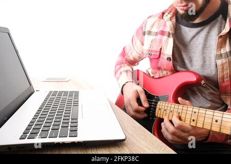 Music College étudiant hippster en chemise à carreaux en damier pratiquant l'exercice de guitare électrique, notes de lecture, ordinateur portable PC. Homme enseignant lui-même, t Banque D'Images