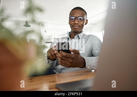 Un jeune homme d'affaires africain envoie des SMS sur son téléphone au travail Banque D'Images