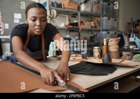 Jeune femme africaine en cuir coupant le cuir à un banc Banque D'Images