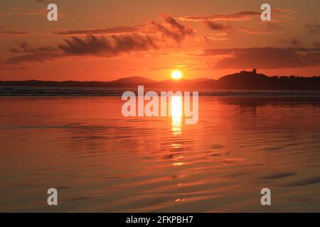 Le soleil couchant silouette le château de Criccieth et projette de magnifiques reflets orange sur le sable ondulé de Black Rock Beach (paysage). Banque D'Images